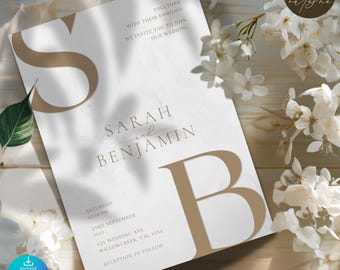 May include: A wedding invitation with the names "Sarah and Benjamin" in elegant typography. The invitation features a large "S" and "B" in a complementary color, with details including the date, time, and location. White flowers and a wooden surface provide a soft background.