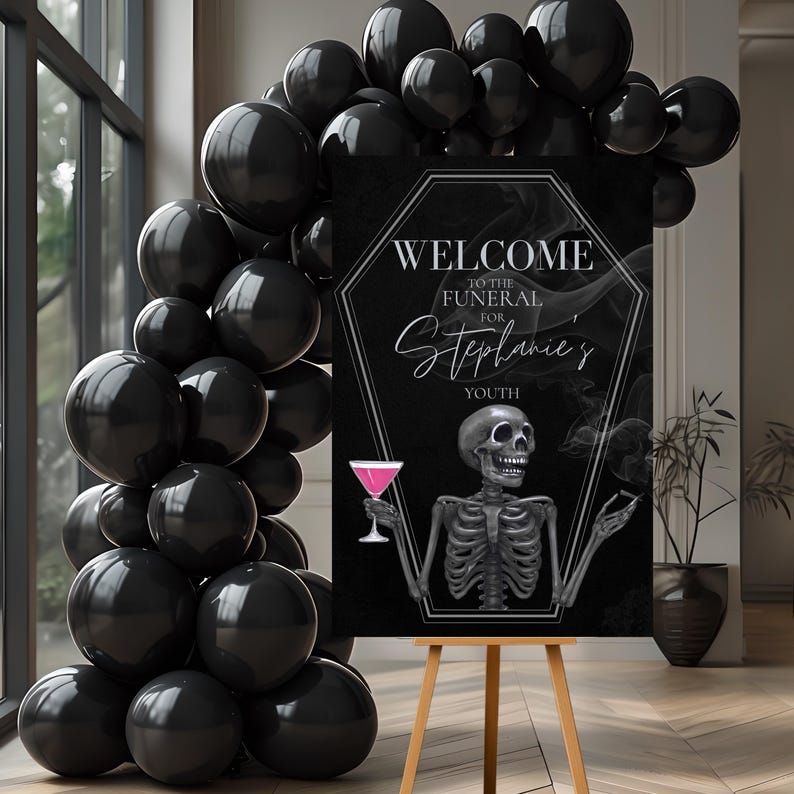 May include: A black sign on a wooden easel with the text "WELCOME TO THE FUNERAL FOR Stephanie's YOUTH". The sign features a skeleton holding a pink cocktail. Black balloons are arranged around the sign.