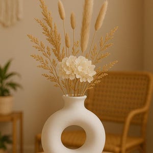 Peut inclure: Vase en céramique blanche avec une grande ouverture circulaire au centre, remplie d'herbe de la pampa séchée et d'hortensias blancs.