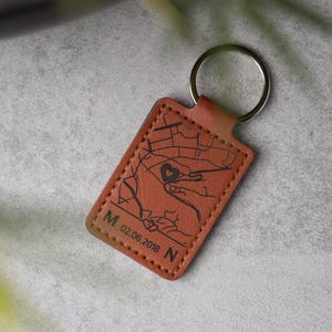 Könnte beinhalten: Rechteckiger, brauner Leder-Schlüsselanhänger mit silbernem Schlüsselring. Er zeigt ein Kartendesign mit einem Herz und dem Datum 02.06.2018 sowie den Buchstaben M und N. Die Kanten sind genäht.