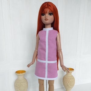 May include: A doll with long red hair wearing a pink dress with white trim. The dress has a sleeveless design with a white vertical stripe down the front and a white horizontal stripe at the hem. The doll is standing in front of a white wall.