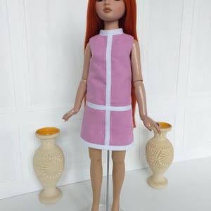 May include: A fashion doll with long red hair and a pink dress with white trim. The doll is wearing white shoes with red accents. Two beige vases with yellow rims are on either side of the doll.