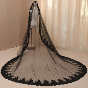 May include: A long, black bridal veil with intricate lace detailing along the edges. The veil is displayed on a mannequin, showcasing its length and delicate design. The lace trim adds a touch of elegance to the sheer fabric.