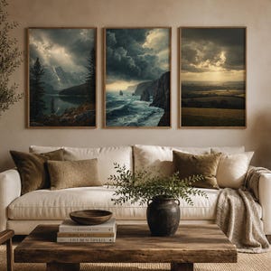 Peut inclure: Trois impressions d'art encadrées représentant des paysages avec des ciels dramatiques et des scènes naturelles. L'œuvre présente un lac de montagne, des falaises côtières et un paysage rural. Les impressions sont au-dessus d'un canapé blanc avec des coussins et une table basse en bois.
