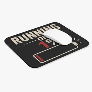 Peut inclure: Un tapis de souris rectangulaire noir avec le texte blanc RUNNING ON et un grand 1% rouge accompagné d'une icône de batterie. Une souris d'ordinateur blanche est posée sur la surface du tapis, dont le motif présente une texture vieillie et usée.