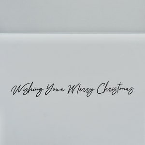 Puede incluir: Una tarjeta de felicitaci&oacute;n blanca con el texto "Wishing You a Merry Christmas" en elegante escritura negra. La tarjeta est&aacute; abierta, revelando un interior en blanco y un dise&ntilde;o simple y limpio, perfecto para mensajes navide&ntilde;os.