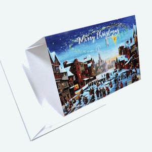 Puede incluir: Una tarjeta de Navidad plegada que representa una escena de pueblo nevado con figuras, edificios y la frase "Merry Christmas". El interior de la tarjeta es blanco.