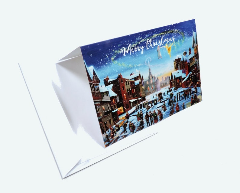 Puede incluir: Una tarjeta de Navidad plegada que representa una escena de pueblo nevado con figuras, edificios y la frase "Merry Christmas". El interior de la tarjeta es blanco.