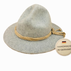 May include: A light gray fedora-style hat with a wide brim and a tan rope band. The hat has a tag that reads "HANDMADE IN GERMANY".