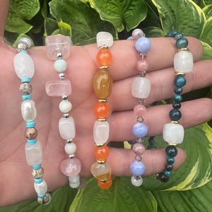 May include: Five gemstone and pearl bracelets in a variety of colours. The bracelets feature white, pink, orange, blue, and green beads. Each bracelet has a unique design with different bead shapes and sizes, suitable for everyday wear.