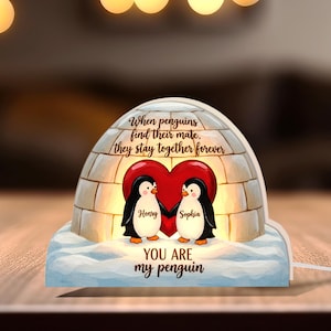 May include: A lighted igloo-shaped night light featuring two penguins inside a red heart. The text reads "When penguins find their mate, they stay together forever." The penguins are named Henry and Sophia. The base says "YOU ARE my penguin."