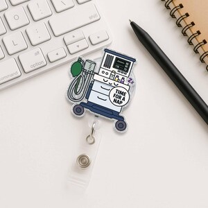 May include: A silver glitter badge reel with a cartoon illustration of a medical breathing machine with the text "Time for a Nap".