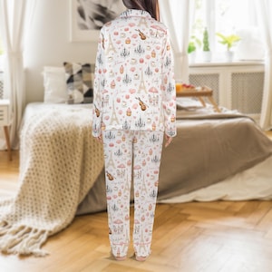 May include: White pajama set with a repeating pattern of Parisian icons, including the Eiffel Tower, chandeliers, and cafe scenes in pink and brown. The long-sleeved top and pants are visible.