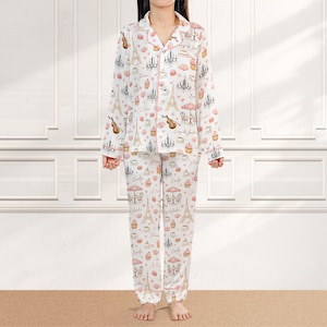May include: White pajama set with a pink trim, featuring a Parisian theme. The set includes a button-down shirt and pants, adorned with Eiffel Towers, chandeliers, and pastries. The design incorporates musical instruments and cafe scenes.
