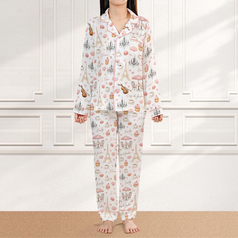 May include: White pajama set with a pink trim, featuring a Parisian theme. The set includes a button-down shirt and pants, adorned with Eiffel Towers, chandeliers, and pastries. The design incorporates musical instruments and cafe scenes.