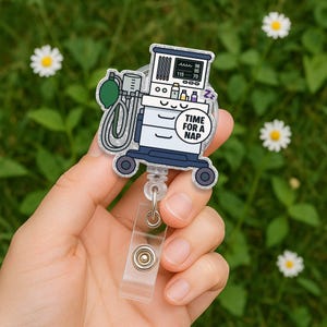 May include: A silver glitter badge reel with a cartoon image of a medical ventilator with the text "Time for a Nap" on a blue circle. The ventilator has a face with eyes and a mouth.