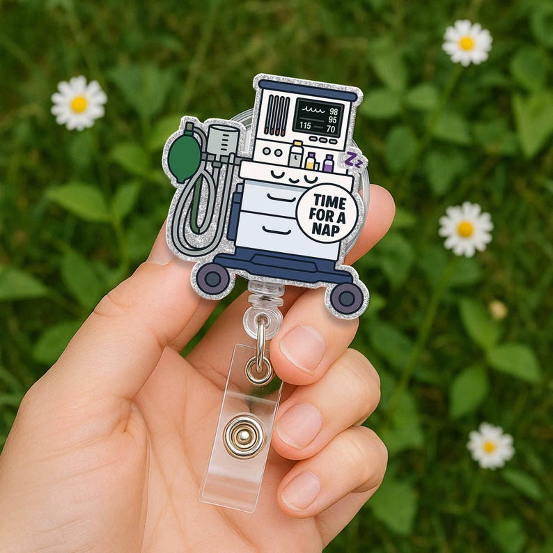 May include: A silver glitter badge reel with a cartoon image of a medical ventilator with the text "Time for a Nap" on a blue circle. The ventilator has a face with eyes and a mouth.