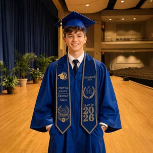 May include: A smiling graduate in a blue graduation gown and cap, with a gold tassel. The sash reads "Computer Science" and "Class of 2026". The graduate is standing in a large auditorium with rows of seats.