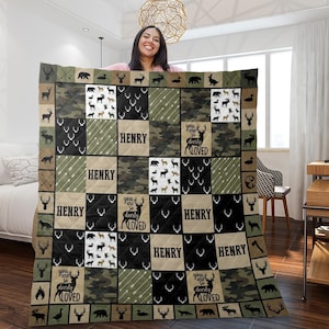 May include: A personalized quilt with a patchwork design featuring deer, arrows, and camouflage patterns. The quilt includes the name "HENRY" and the phrase "you are so deerly LOVED" in a decorative font. The color palette includes shades of green, black, and tan.