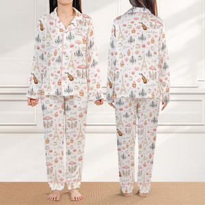 May include: White pajama set with a pink trim, featuring a repeating pattern of Parisian icons like the Eiffel Tower, chandeliers, and musical instruments. The long-sleeved top and pants are made of a soft material.