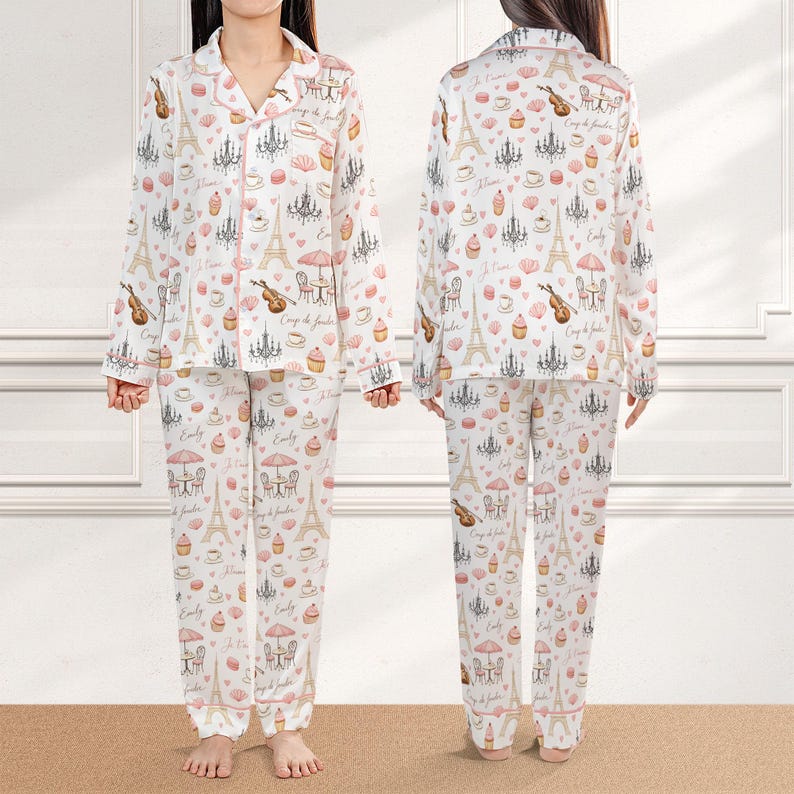 May include: White pajama set with a pink trim, featuring a repeating pattern of Parisian icons like the Eiffel Tower, chandeliers, and musical instruments. The long-sleeved top and pants are made of a soft material.
