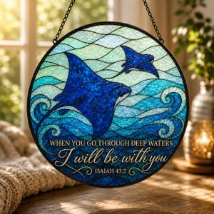May include: A circular stained glass suncatcher featuring two deep blue manta rays swimming through stylized turquoise and light blue ocean waves. The text reads: WHEN YOU GO THROUGH DEEP WATERS I will be with you ISAIAH 43:2 in gold lettering.
