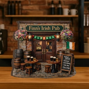 Könnte beinhalten: Ein Miniaturmodell des Finn's Irish Pub mit Ziegelfassade, grünem Schild und einem Banner mit der Aufschrift Slainte. Die Szene umfasst zwei runde Tische mit Hockern, Biergläsern, Holzfässern, einer Kreidetafel als Menü und Blumenampeln.