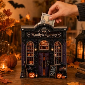 May include: A dark-themed wooden money box shaped like a miniature building labeled Emily's Library. The structure features arched windows, a central door, and miniature pumpkins. It includes a slot at the top for inserting a 100 dollar bill.