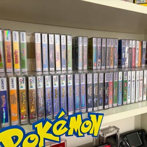 Könnte beinhalten: Eine Sammlung von Vintage-Videospielkassetten und -hüllen, darunter Game Boy- und Nintendo DS-Titel. Die Spiele sind auf Regalen angeordnet, mit dem Wort "Pokémon" in einem gelb-blauen Schild unten.
