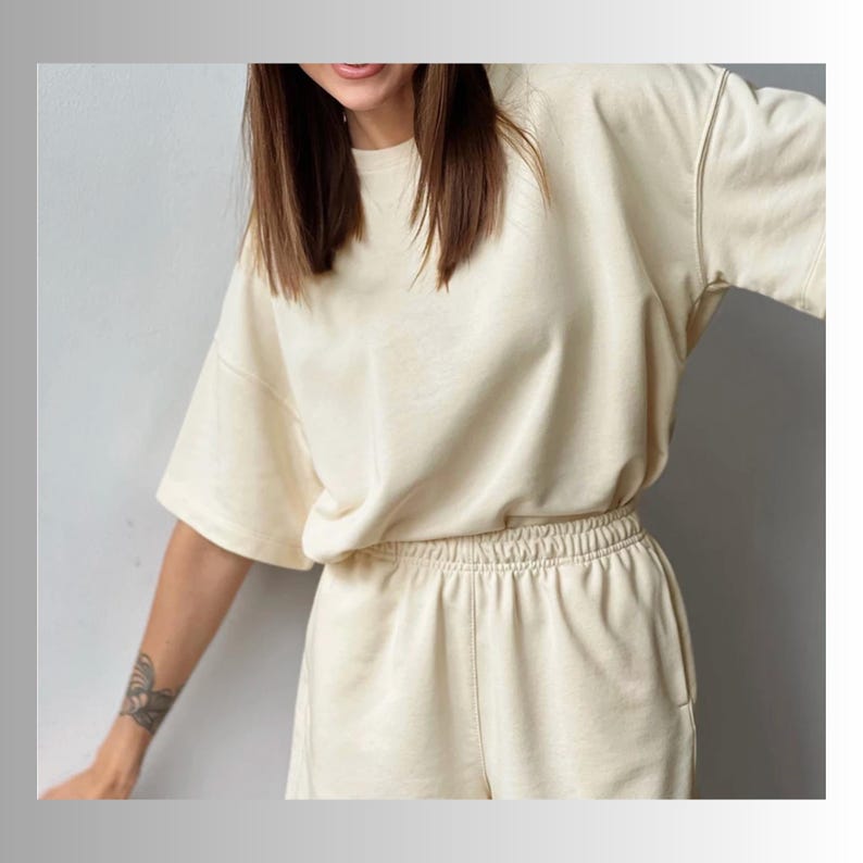 May include: A cream-colored, short-sleeved, oversized t-shirt and matching shorts set. The set is made of a soft, comfortable fabric.