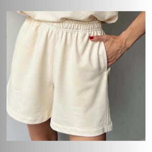 May include: Cream colored, soft, cotton shorts with an elastic waistband. The shorts have a relaxed fit and are perfect for casual wear.