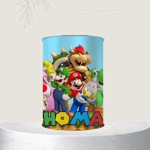 May include: A cylindrical container with a light blue background featuring a colorful graphic of Mario, Luigi, Princess Peach, Bowser, Yoshi, and other characters. The word "HOMA" is printed in large, colorful letters at the bottom.