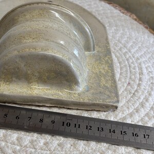 May include: A handmade ceramic soap dish in a light beige color. The dish has a curved, cylindrical holder and a rectangular base. A ruler shows the dish is approximately 6 inches long.