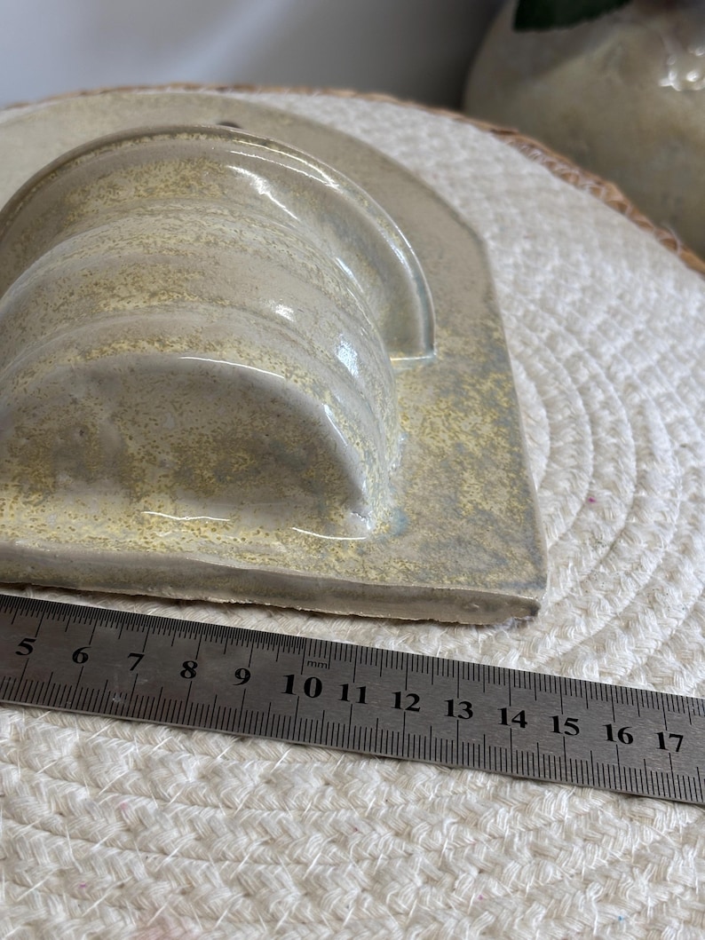 May include: A handmade ceramic soap dish in a light beige color. The dish has a curved, cylindrical holder and a rectangular base. A ruler shows the dish is approximately 6 inches long.