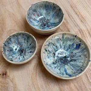 Könnte beinhalten: Drei Keramikschalen mit einem gesprenkelten blauen, grünen und roten Design. Die Schalen sind unterschiedlich groß, mit einer kleinen Schale, einer mittelgroßen Schale und einer flachen Schale. Die Schalen haben eine cremefarbene Außenseite und ein glänzendes Finish.