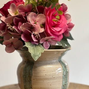 Könnte beinhalten: Eine Keramikvase mit beigefarbenem Sockel und zwei vertikalen grünen Streifen enthält ein lebendiges Arrangement aus rosa und roten Blumen. Die Blumen umfassen Rosen und Hortensien, mit grünem Laub.