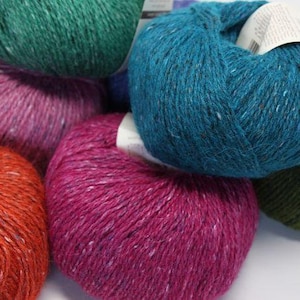 May include: A collection of six yarn skeins in various colors, including teal, pink, orange, and green. The yarn is a tweed blend with a speckled appearance.