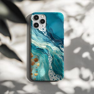 Könnte beinhalten: Eine teal- und blaue Handyhülle mit einem fließenden Aquarelldesign. Die Hülle hat goldene Akzente und einen Marmoreffekt mit einer Mischung aus hellen und dunklen Blautönen. Das Design ähnelt Meereswellen.