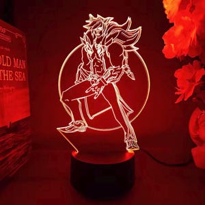 May include: A red LED lamp featuring a stylized character design. The figure is outlined in white, with a dynamic pose. The lamp sits on a black base, and the background is a deep red. The design is reminiscent of a video game character.