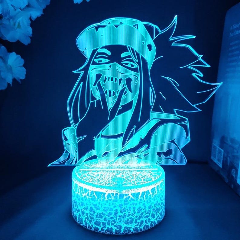 Puede incluir: Una luz nocturna LED azul que presenta un personaje de anime estilizado con una m&aacute;scara y un sombrero. El personaje est&aacute; iluminado con una luz azul brillante, y la base tiene una apariencia agrietada y texturizada. La luz est&aacute; sobre un fondo oscuro.