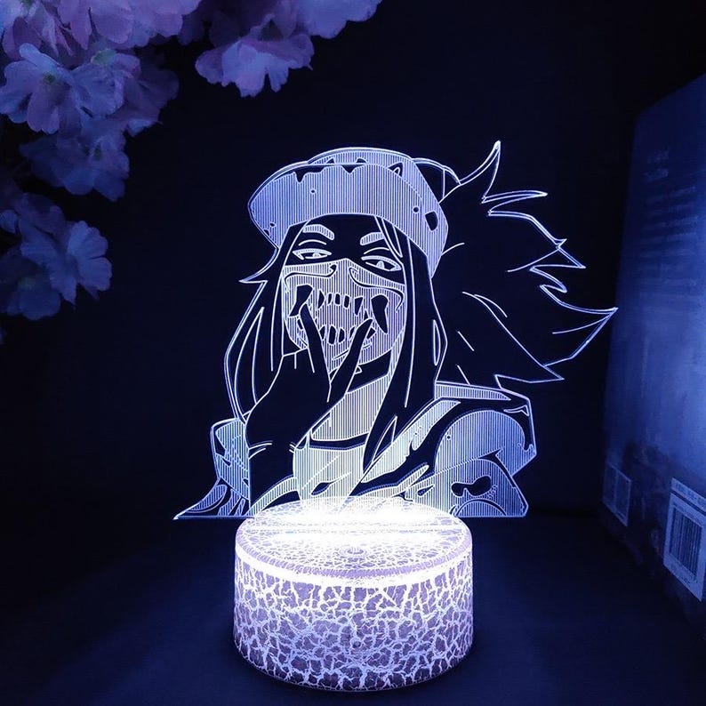 Puede incluir: Luz de noche LED brillante con un personaje de anime estilizado con m&aacute;scara y sombrero. El personaje est&aacute; representado en l&iacute;neas blancas sobre un fondo oscuro, con una base redonda y texturizada que emite una luz suave y fr&iacute;a. Dise&ntilde;o moderno y art&iacute;stico.