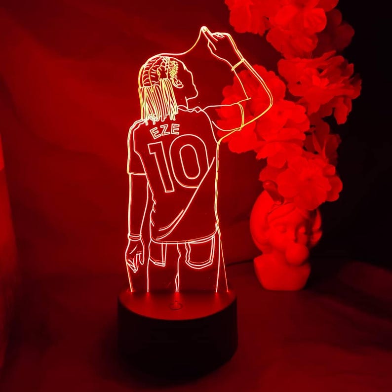 May include: A red-illuminated 3D lamp depicting a footballer in a jersey with "EZE" and the number "10". The lamp sits on a black base, with a red backdrop and decorative features.