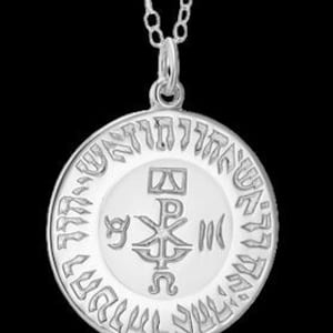 May include: A silver circular pendant necklace featuring a central Chi Rho symbol with Greek letters Alpha and Omega, surrounded by a border of engraved Hebrew text. The pendant hangs from a delicate silver chain against a black background.