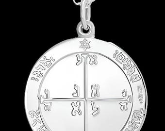 May include: A silver pendant necklace with a circular charm. The charm features an engraved design with Hebrew letters and symbols, including a Star of David. The pendant hangs from a delicate silver chain.