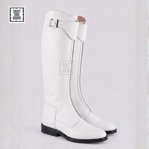 May include: A pair of white leather riding boots. The boots have a tall shaft, a buckle detail at the top, and a black sole. The boots are displayed on a white background. The logo "Craft Edge Goods" is visible in the upper left corner.