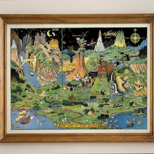 May include: A framed, detailed map illustration titled The Land of Make Believe, featuring a vibrant landscape with mountains, a winding river, a large central tree, castles, and various small figures. The artwork is enclosed in a wooden frame.