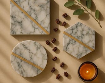 May include: Marble coasters in square, round, and hexagonal shapes with gold accents. Coffee beans and a lit candle are scattered around the coasters. A sprig of green leaves adds a natural touch to the arrangement.