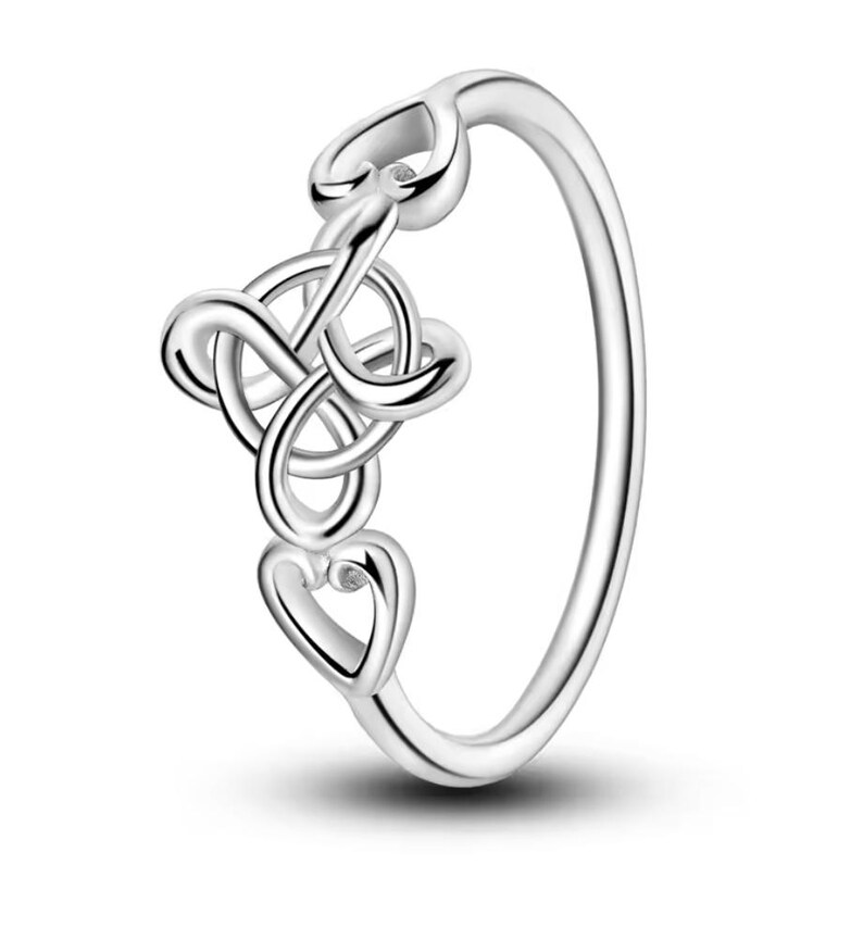Op de afbeelding: Een zilveren ring met een delicaat ontwerp met in elkaar verweven harten en een kleine, heldere steen.