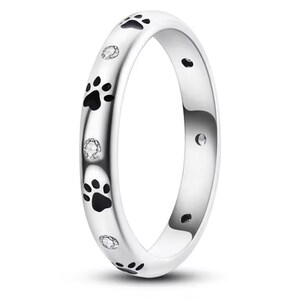 Op de afbeelding: Een zilveren ring met zwarte poot afdrukken en kleine heldere diamanten rond de band.