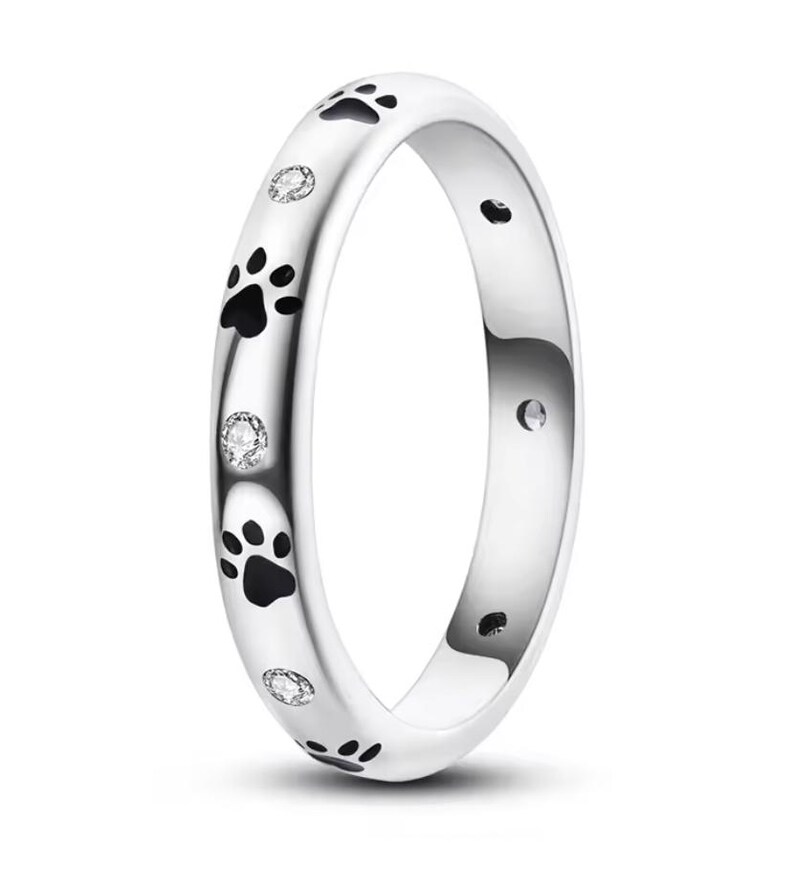 Op de afbeelding: Een zilveren ring met zwarte poot afdrukken en kleine heldere diamanten rond de band.